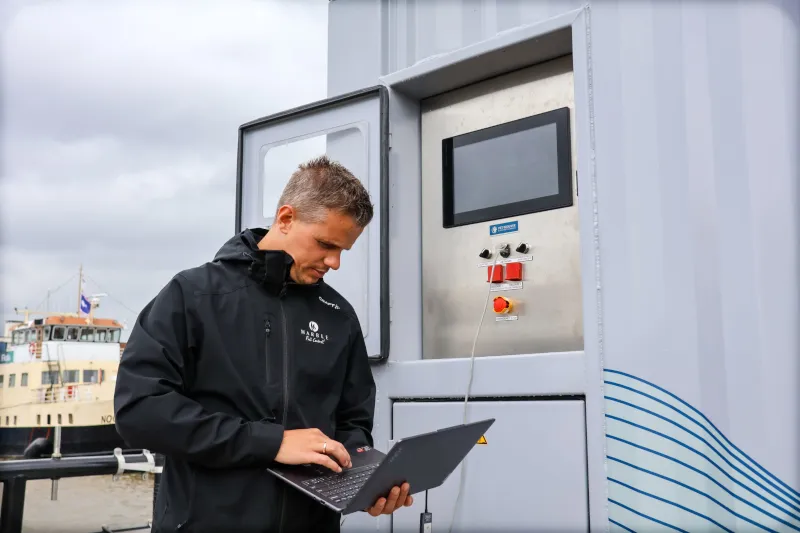 Marble engineer working on a laptop beside a stainless steel control panel on the quay
