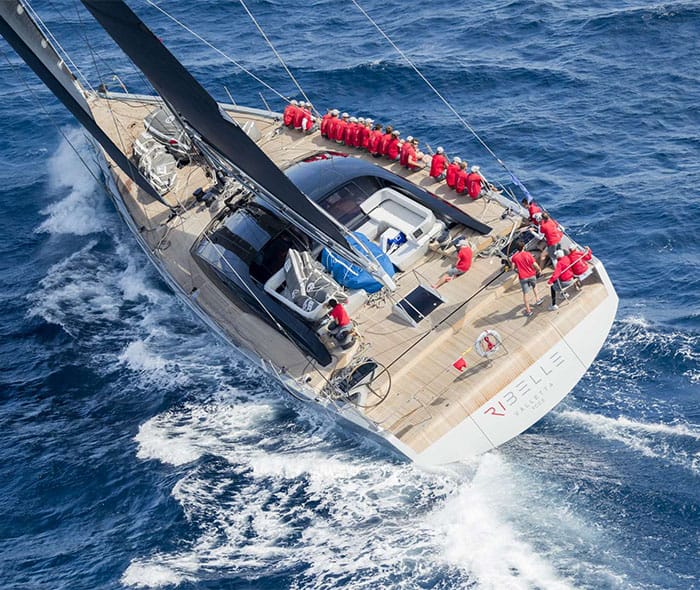 Sailing yacht Ribelle heeling at sea with crew in red along the rail