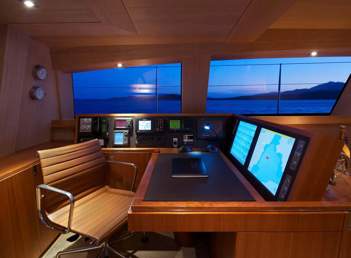 Yacht wheelhouse at dusk with wooden bridge console, navigation screens and helm chair